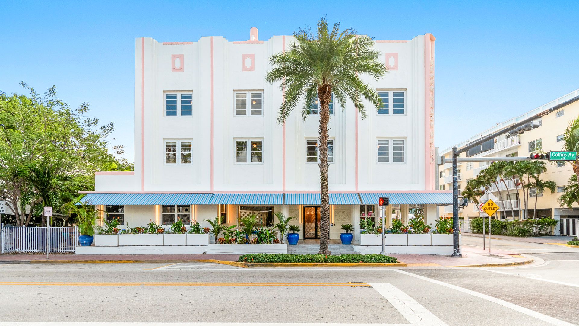 la fachada Art Déco blanca de tres plantas con detalles rosas y una palmera